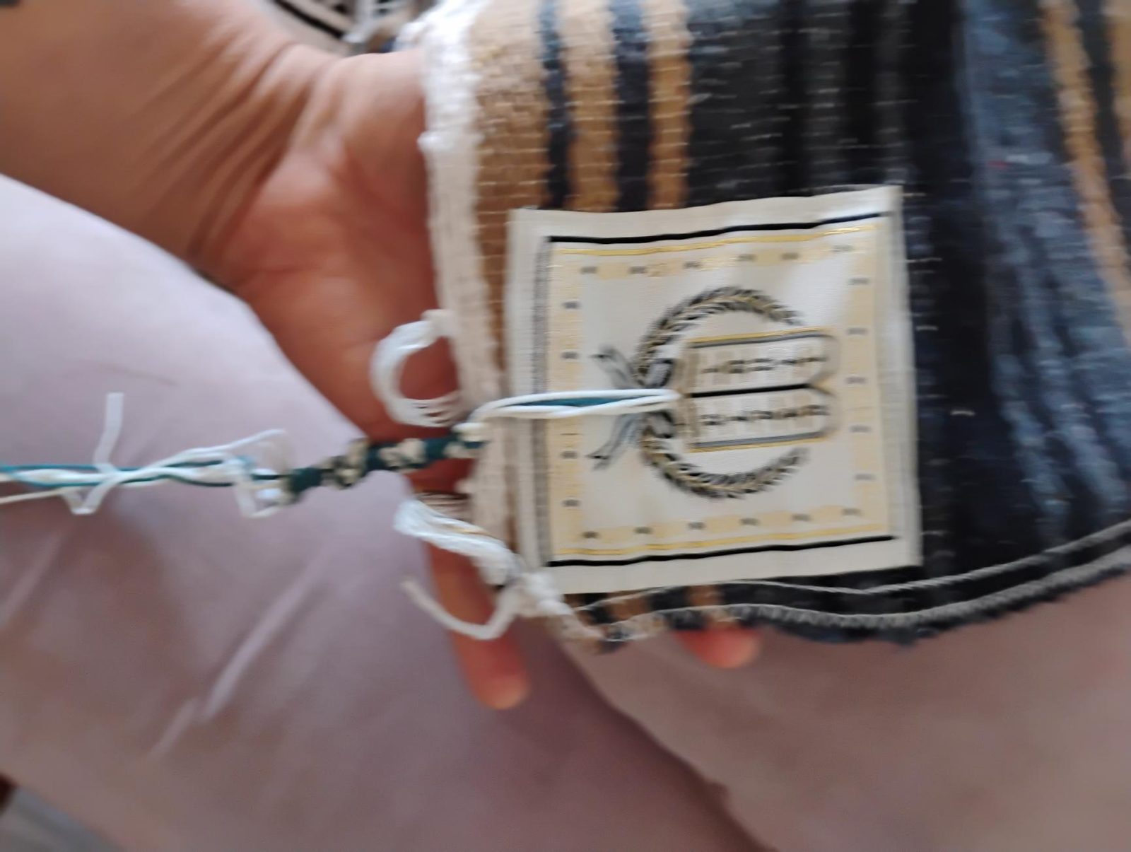Placa de esquina bordada con las tablas dentro de una corona de laurel. Los tzitzit, con un hilo azul, pasan por la placa.